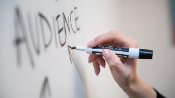 Closeup of a hand writing "audience" on a whiteboard.