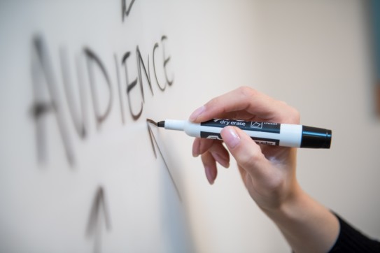 Closeup of a hand writing "audience" on a whiteboard.