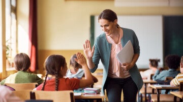 Happy elementary school administrator giving high-five to a student during class in the classroom.