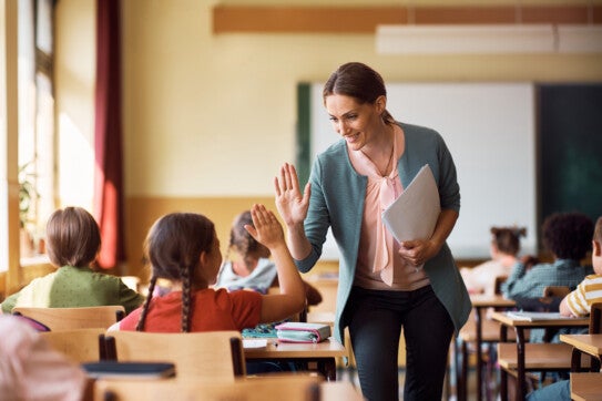 Happy elementary school administrator giving high-five to a student during class in the classroom.